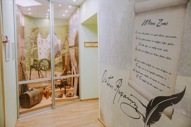 Ienākot muzejā apmeklētāju sagaida A. Rupaiņa autogrāfs uz dzimto māju "Pūrisku" fona